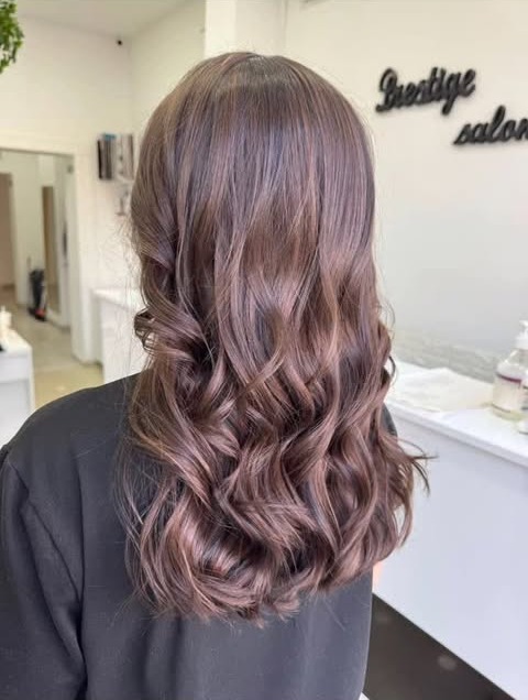 Clientă cu bucle ciocolatii în fața logo-ului Prestige Salon de pe perete